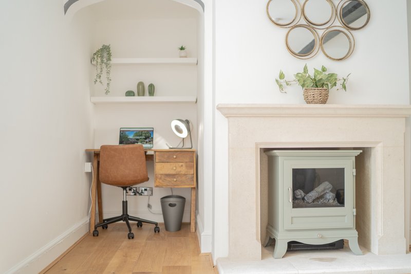 Bright living room with fireplace, desk nook, shelving and decorative mirrors and plants