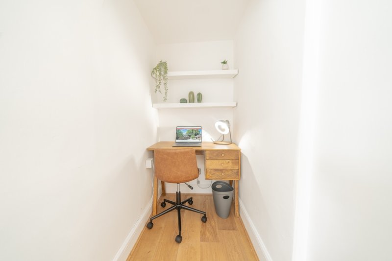 Narrow home office with wooden desk, office chair, shelving, and potted plants