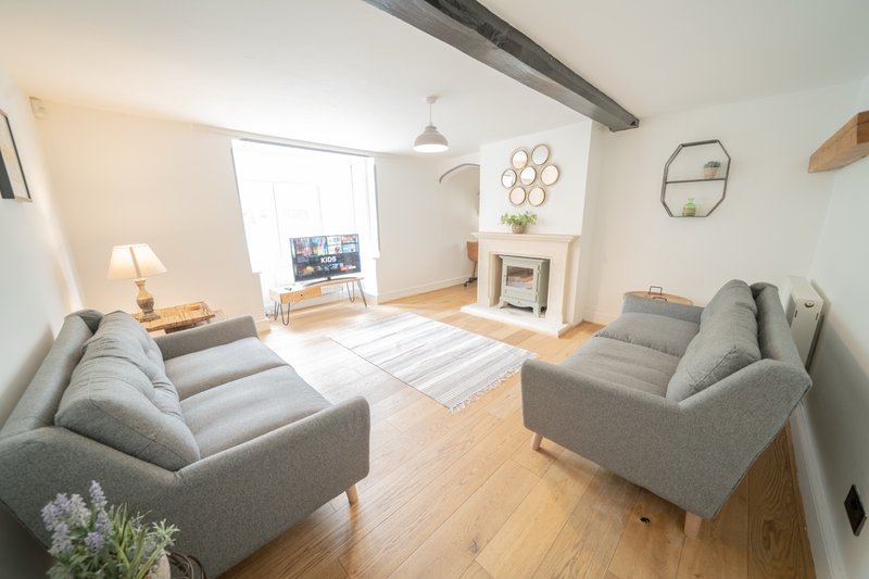Bright living room with two grey sofas, wooden flooring, fireplace and large window