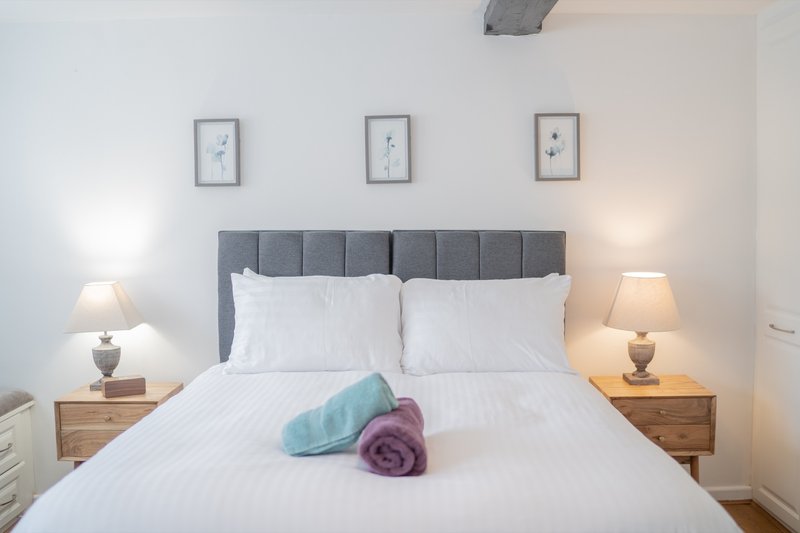 Modern bedroom with grey upholstered headboard, white bedding, wooden nightstands and table lamps