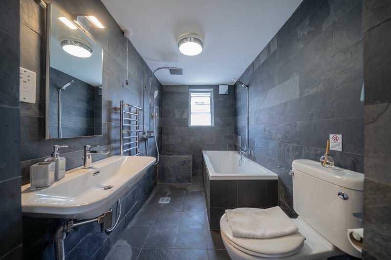 Modern bathroom with dark tile walls, double sink vanity, bathtub and toilet