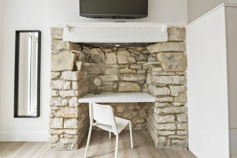 Stone fireplace alcove with white chair, desk space, and mounted TV above