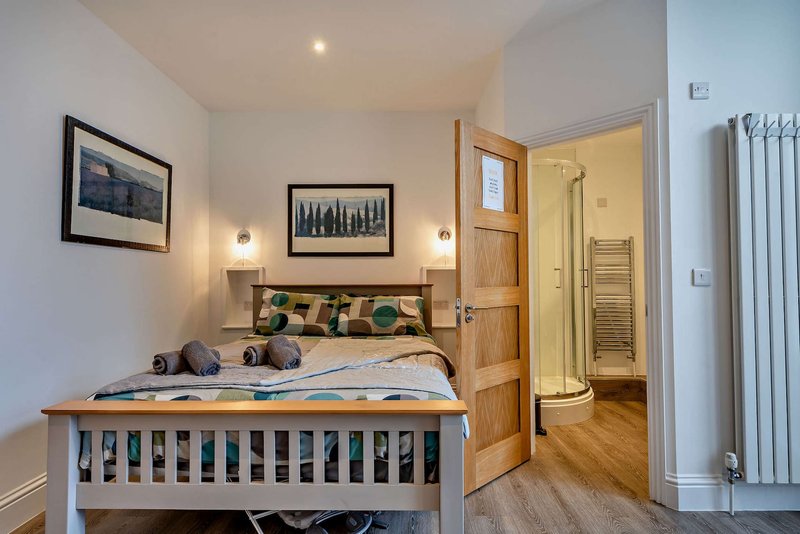 Modern bedroom with double bed, wooden headboard, framed artwork, and ensuite bathroom visible