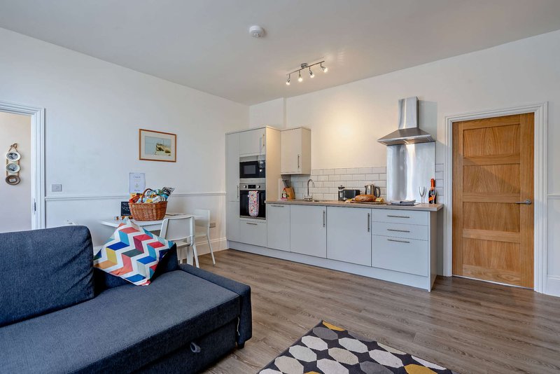 Open-plan living area with kitchen, blue sofa, dining table and wooden door