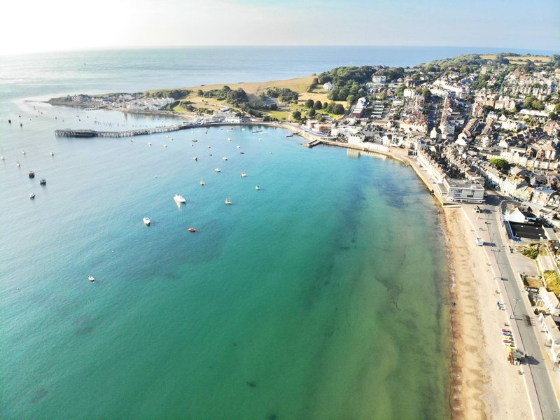 Aerial view of coastal town with sandy beach, turquoise water, and hillside residential buildings