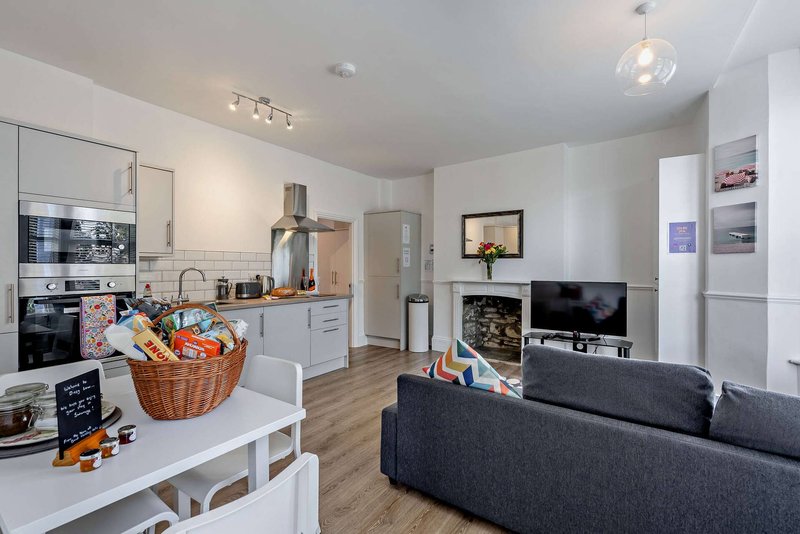 Open-plan kitchen and living room with white cabinetry, dark sofa, and integrated appliances