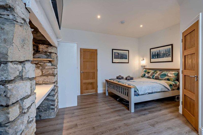 Spacious bedroom with wooden bed frame, stone fireplace, wooden doors and laminate flooring