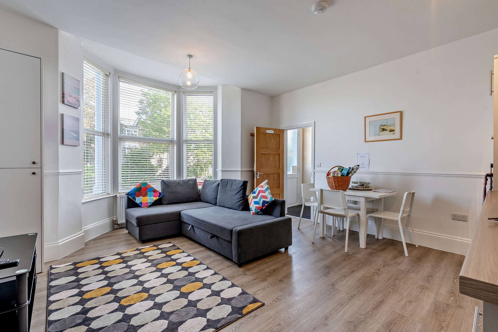 Open-plan living room with dark corner sofa, geometric rug, dining table and large windows