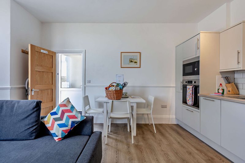 Open-plan living and kitchen area with sofa, dining table, chairs and fitted kitchen units