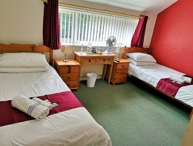 Triple bedroom with three single beds, wooden desk, fan and burgundy accents