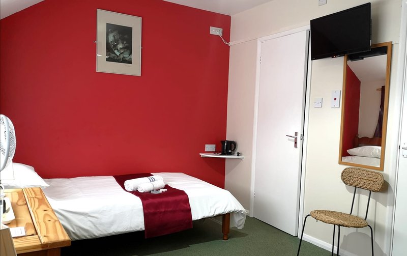 Bedroom with red accent wall, single bed, white bedding, wall-mounted TV, and mirror