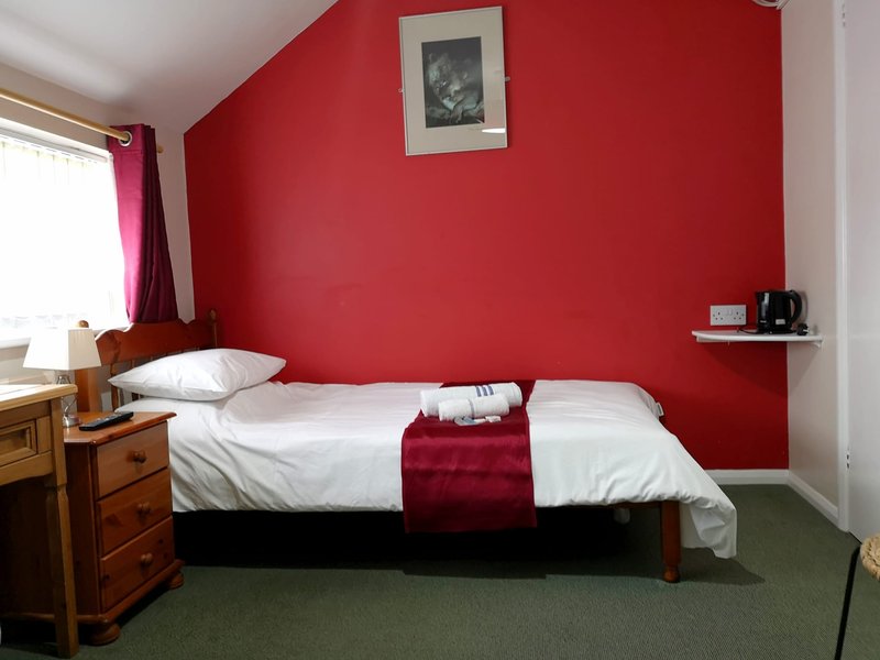 Bedroom with double bed, red walls, wooden furniture, and framed artwork