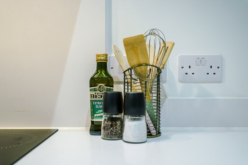 Kitchen counter with olive oil bottle, cooking utensils in holder, and salt and pepper shakers