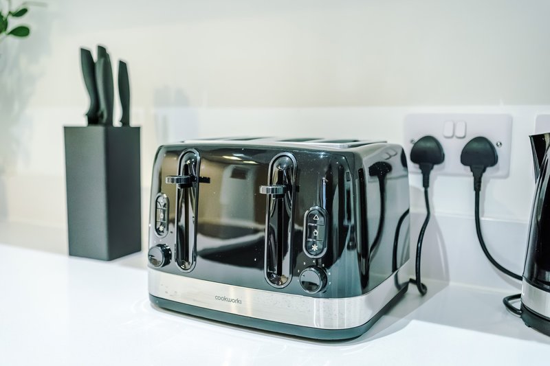 Kitchen countertop with chrome toaster, knife block, and cooking utensils on white surface