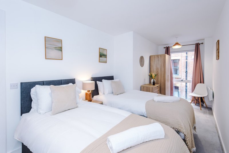 Bright twin bedroom with white bedding, dark headboards, wooden wardrobe and access to ensuite bathroom
