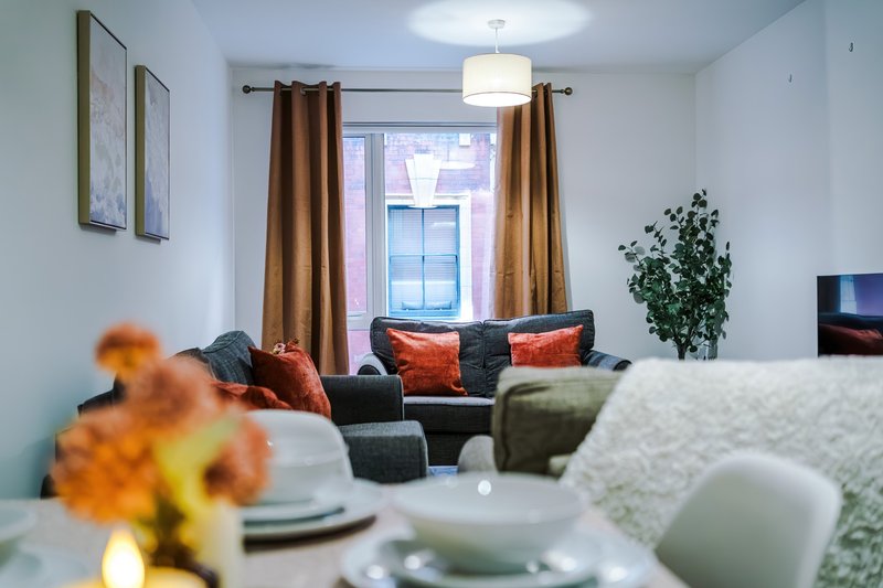Modern living room with gray sofa, orange cushions, plant, and window with brown curtains