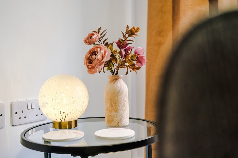 Side table with decorative globe lamp, flower arrangement in vase, and wall outlet
