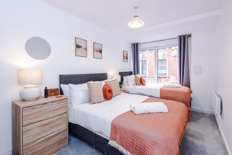 Bright twin bedroom with white walls, two beds with coral bedding, wooden dresser and pendant ceiling light
