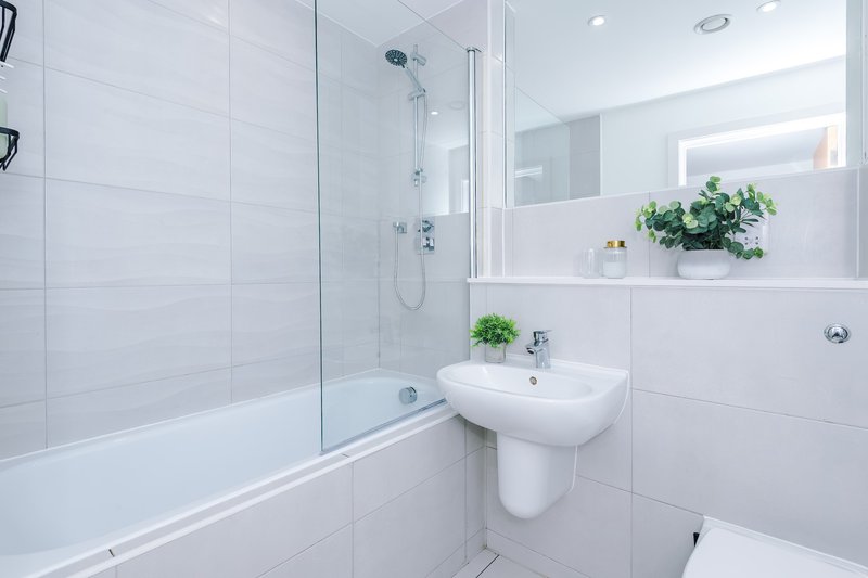 Modern bathroom with white tiles, glass shower enclosure, pedestal sink and potted plants