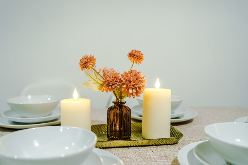 Styled dining table setting with white plates, orange flowers in vase, and lit candles