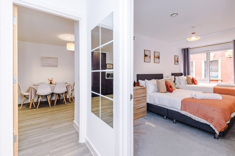 Modern bedroom with twin beds, orange bedding, wooden furniture and open door to dining area
