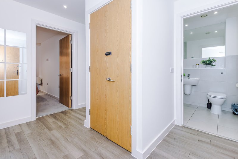 Modern hallway with wooden door, white walls, laminate flooring, and bathroom entrance visible