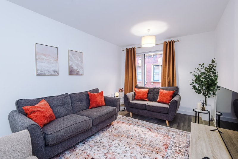 Modern living room with two gray sofas, orange cushions, potted plant and television