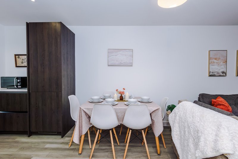 Open-plan living area with dining table, two chairs, kitchenette and sofa with cushions