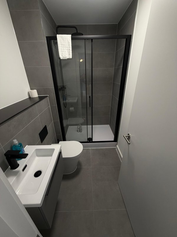 Modern bathroom with toilet, sink, shower enclosure and grey tile flooring