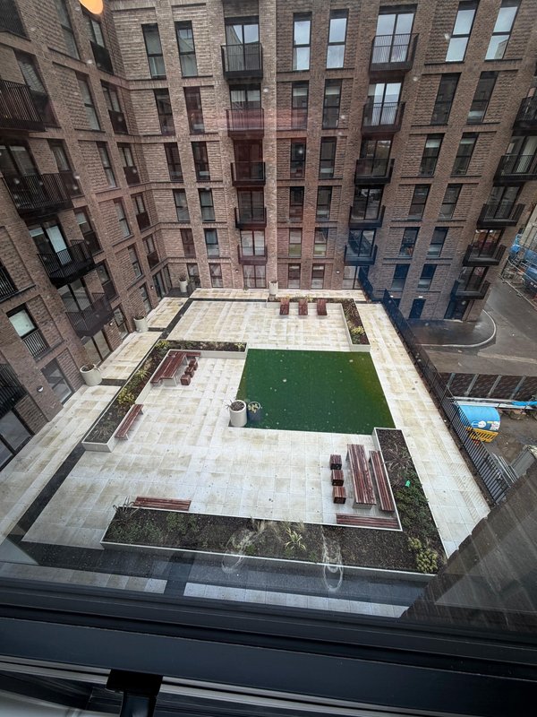 Aerial view of communal courtyard with artificial turf, paving, and brick residential buildings surrounding