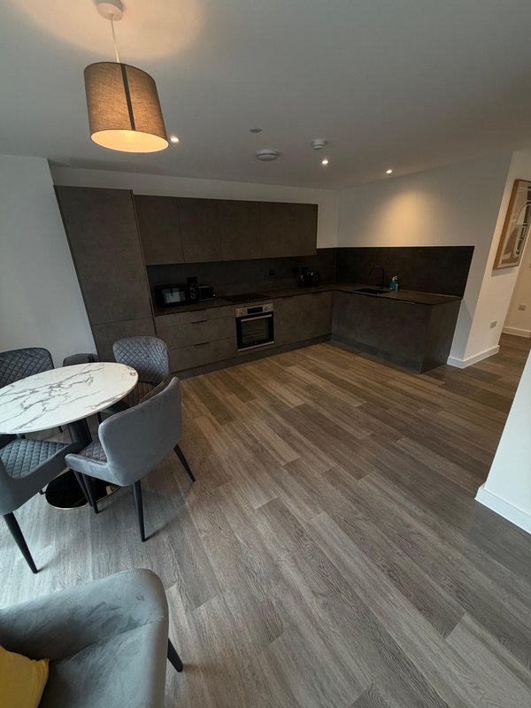 Modern open-plan kitchen and dining area with dark cabinetry, wooden flooring, pendant lighting and seating