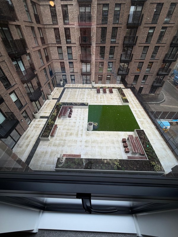Aerial view of modern communal courtyard with paved areas, green lawn and surrounding brick buildings