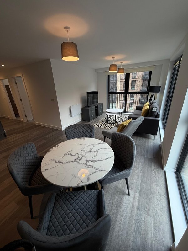 Modern open-plan living area with marble dining table, black chairs, pendant lighting, and city views