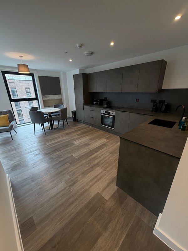 Open-plan kitchen and living area with dark cabinetry, wooden flooring, and dining table
