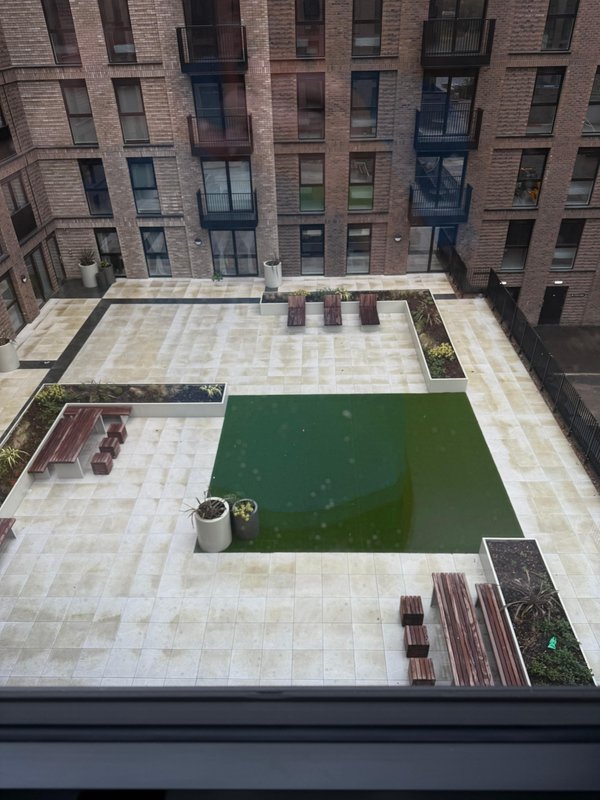 Aerial view of shared courtyard with paved area, artificial grass, and surrounding brick apartment building