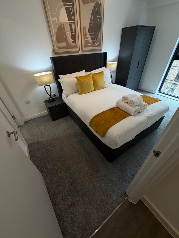 Modern bedroom with double bed, gold and white bedding, black headboard, and abstract wall art