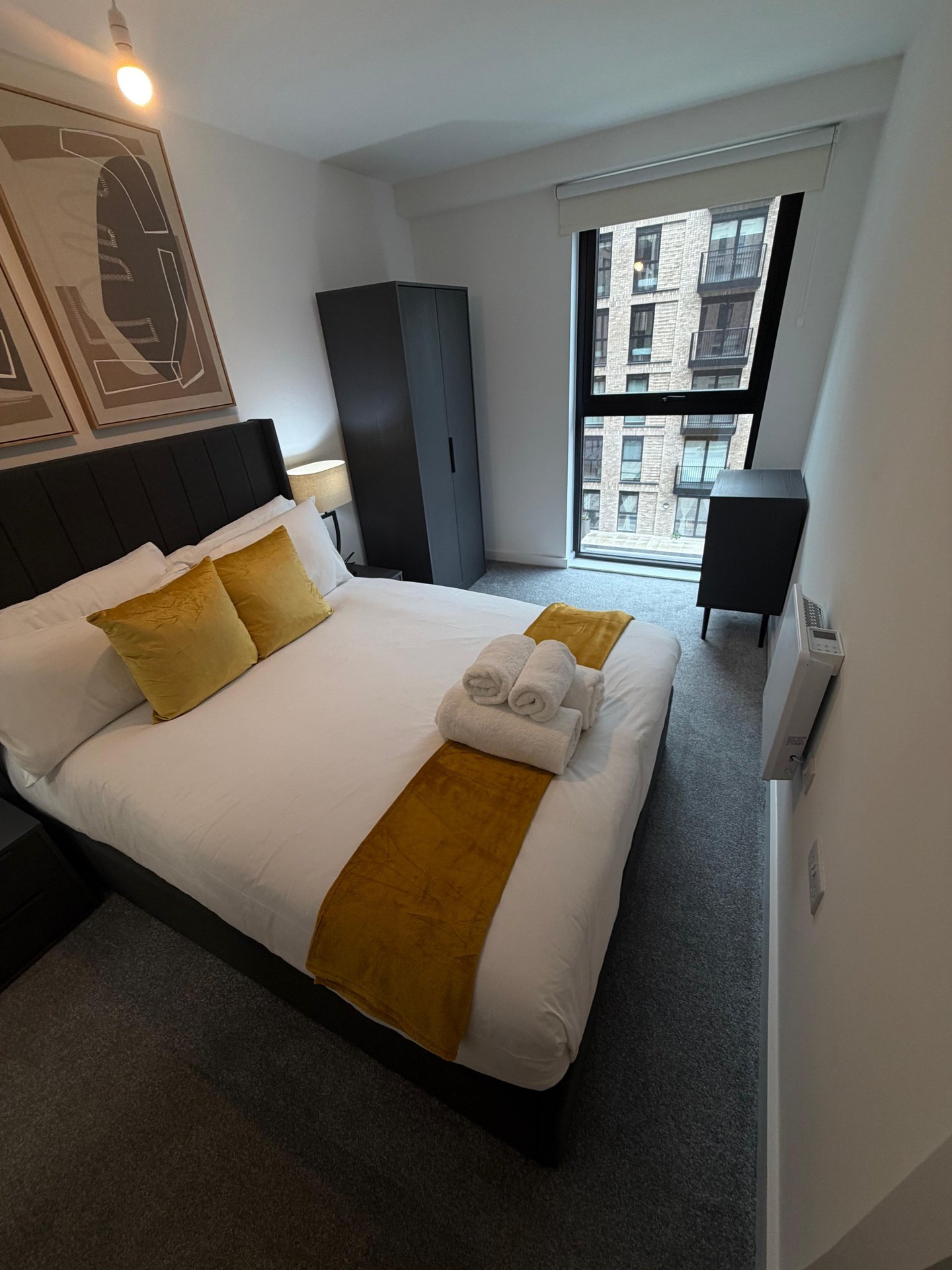 Modern bedroom with double bed, yellow cushions, dark headboard, window with city view