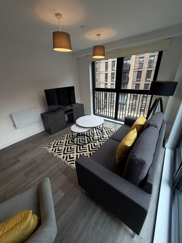 Modern living room with dark sofa, TV stand, geometric rug, pendant lights and balcony doors