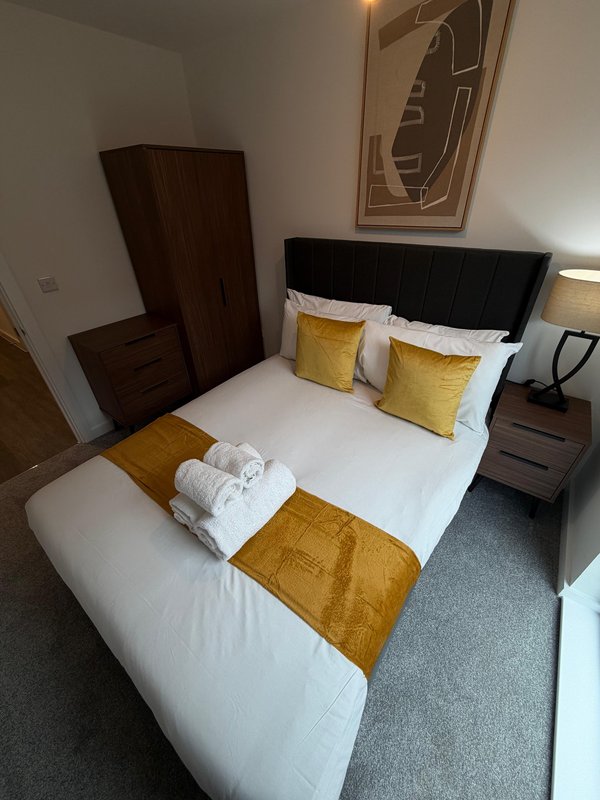 Modern bedroom with double bed, yellow cushions, white linens, dark wood furniture and wall art