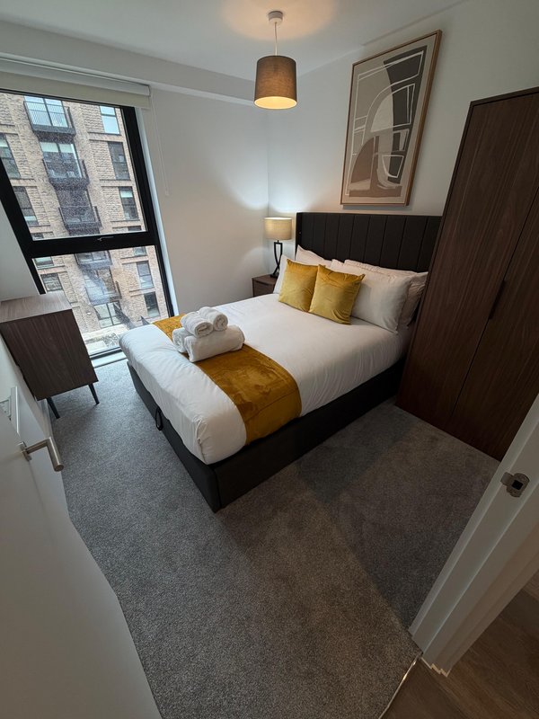 Modern bedroom with double bed, yellow cushions, dark wood furniture and city views
