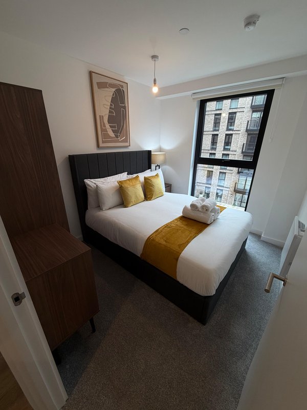 Modern bedroom with double bed, yellow accents, pendant light and city window view