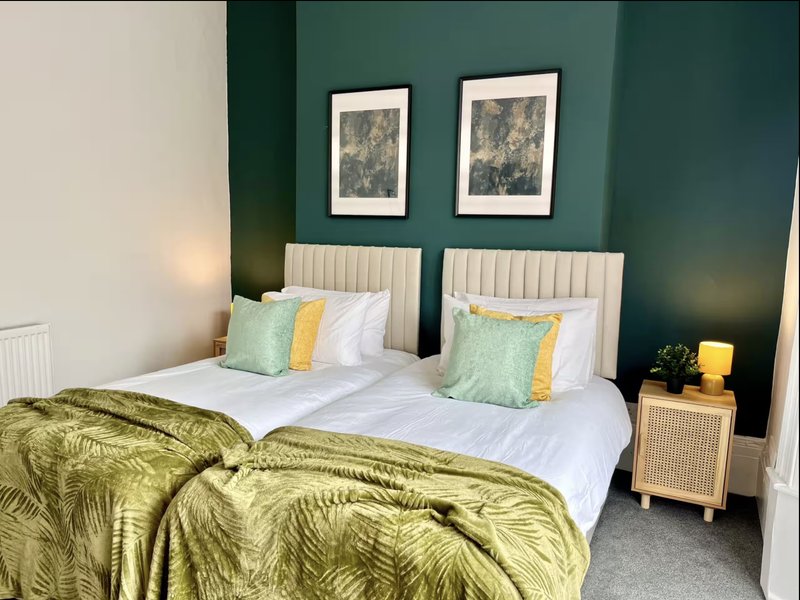 Bedroom with dual beds, green bedding, framed wall art, and cream nightstand.