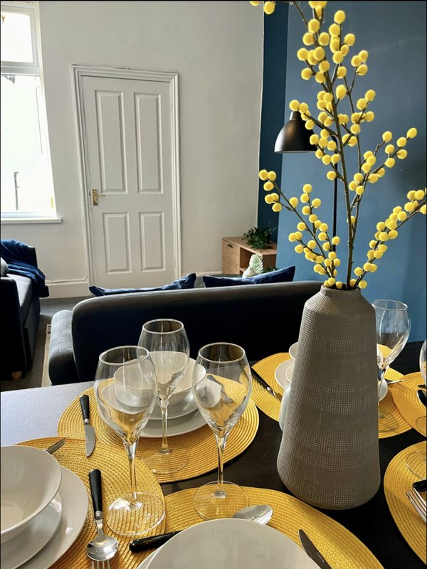 Dining table set with yellow placemats, glasses, and floral arrangement in vase
