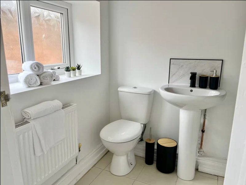 Clean bathroom with toilet, pedestal sink, radiator and window with rolled towels