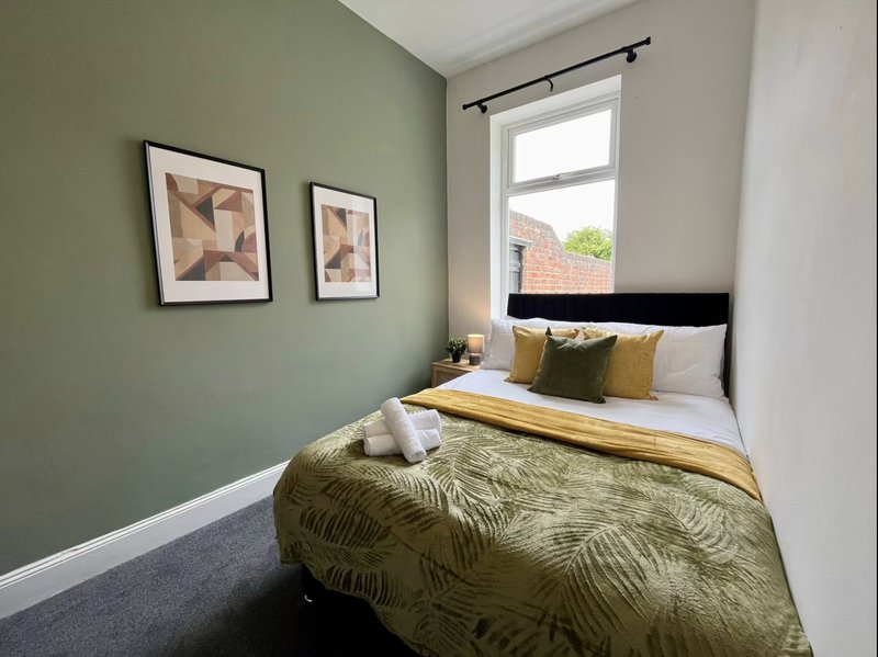 Compact bedroom with double bed, green accent wall, framed artwork and window.