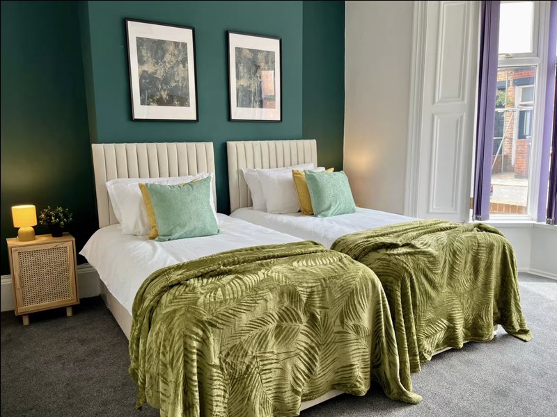 Modern bedroom with twin beds, green bedding, teal accent wall, framed artwork and bright windows