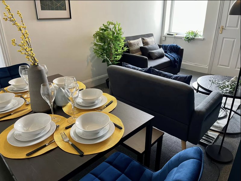 Dining area with set table, yellow placemats, black sofa and blue armchair