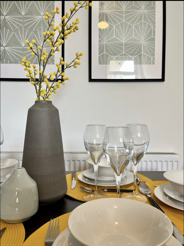 Dining table set with white plates, glasses, cutlery, yellow branches in vase, and framed wall art