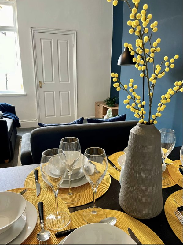 Dining table set with yellow placemats, glasses, and floral centerpiece arrangement