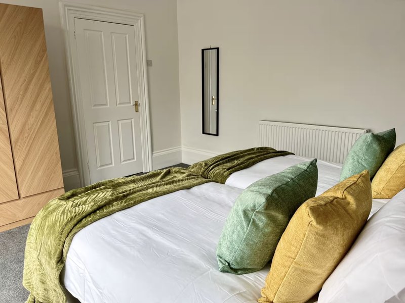 Bright bedroom with double bed, colorful cushions, white door and radiator